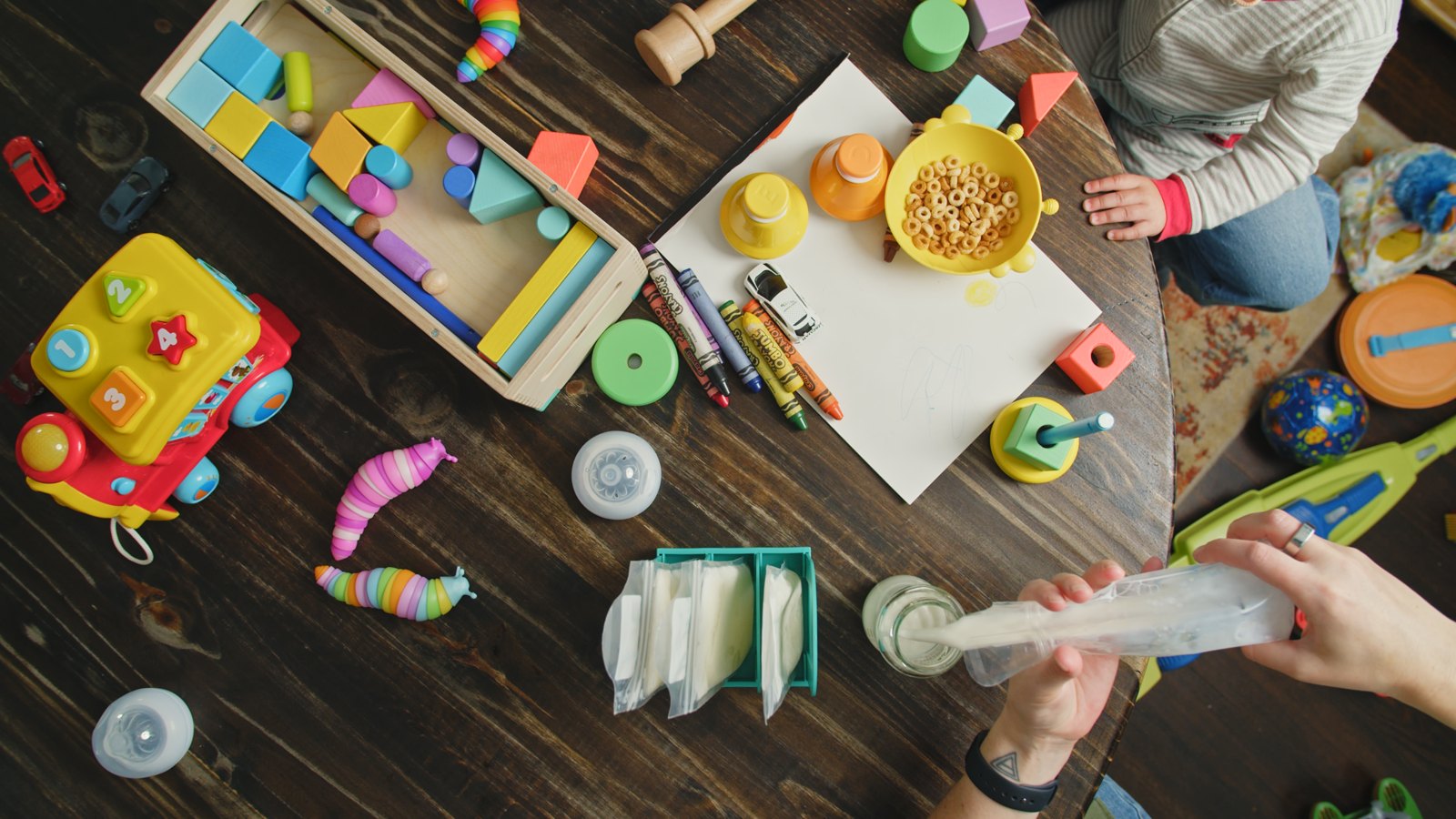 Overhead view of a parent pouring thawed milk at a busy family table with Mylk Mate