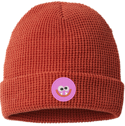 Red knit beanie with a pink smiley face patch on a white background